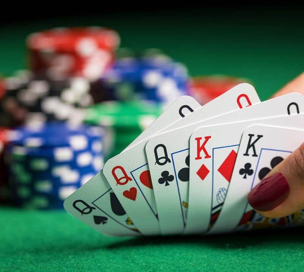 Hand holding playing cards in a fan shape, with colorful poker chips in the background.