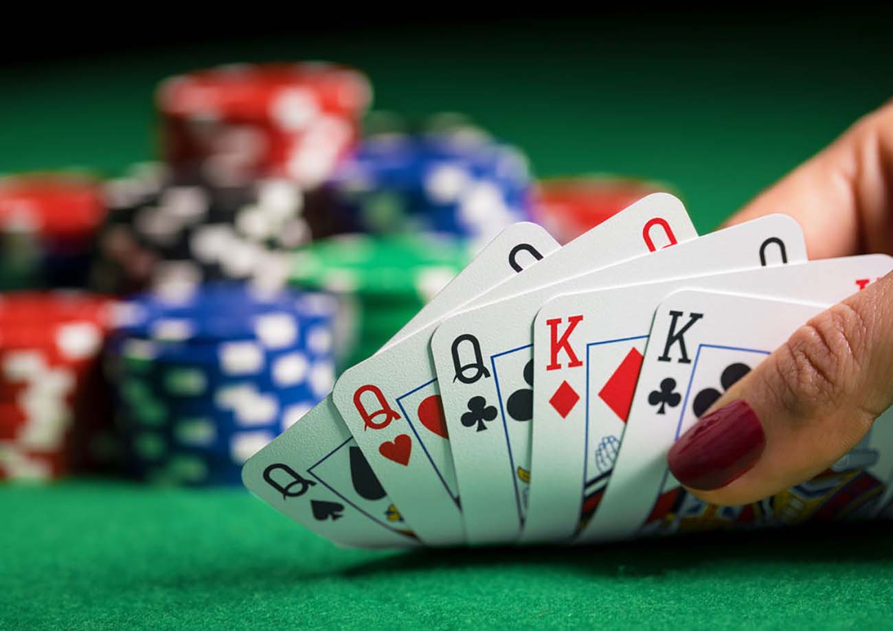 Hand holding playing cards in a fan shape, with colorful poker chips in the background.