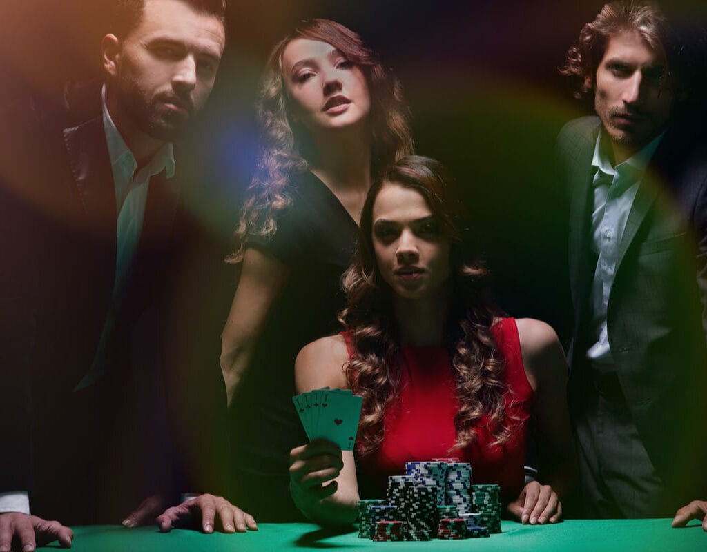 Four people around a poker table, one holding cards.