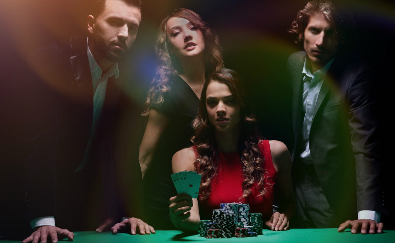 Four people around a poker table, one holding cards.