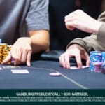 Close-up of two poker players’ arms and hands at a casino table, focused on the game, with stacks of colorful chips in front of them. The table features playing cards and poker chips