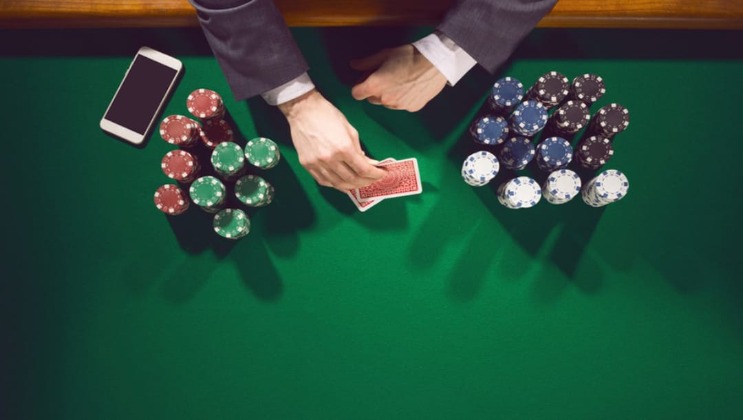 Hands dealing cards on a poker table with chips and a smartphone.