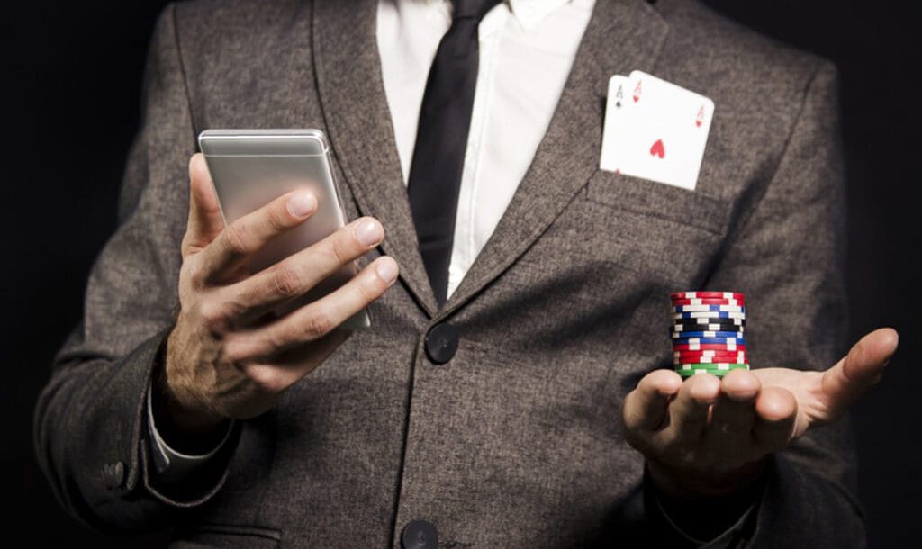 The gambler holds a mobile phone in his right hand and a chip in his left.