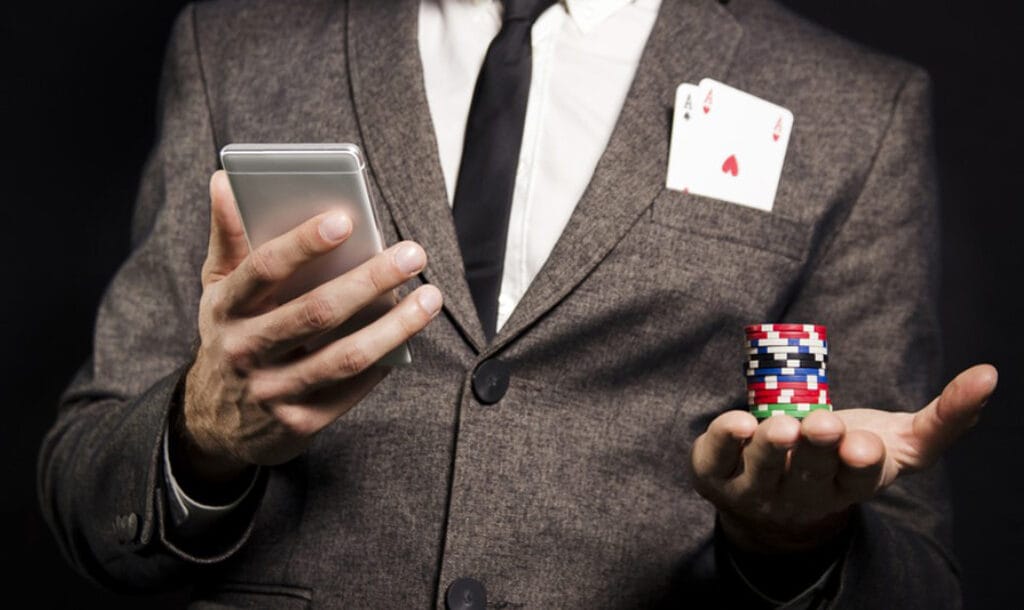 The gambler holds a mobile phone in his right hand and a chip in his left.