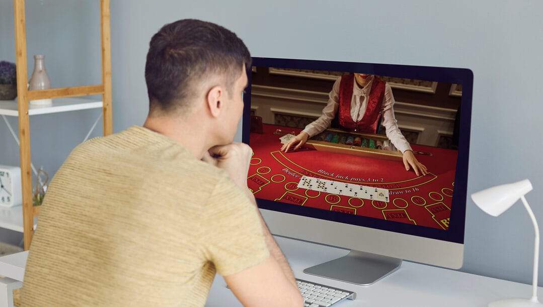 A man sits at a desk with a live poker game on his computer screen.