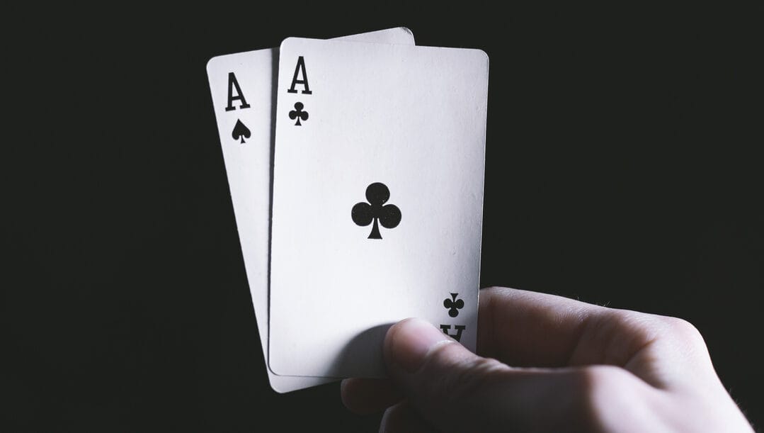 A person holds up a pair of aces on a black background.