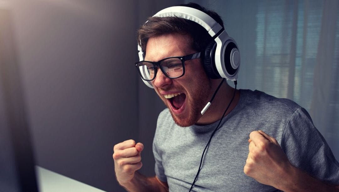 Man sitting at a desk wearing a headset and shouting excitedly while clenching his fists.