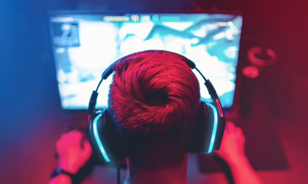 Gamer playing on a desktop wearing a headset in a red-lit room.