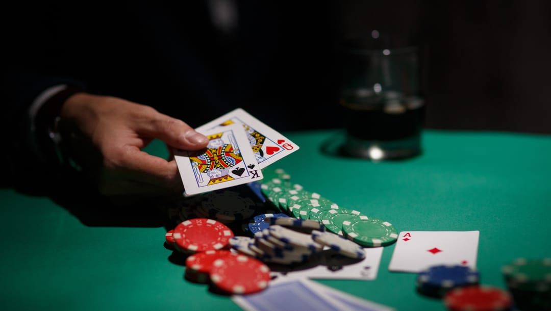 A person holding a King and a Queen in a poker game with chips and cards on the table.