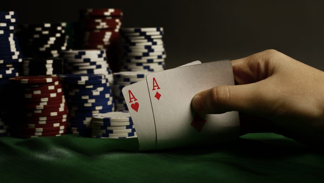 A poker player reveals two Aces with casino chips in the background.