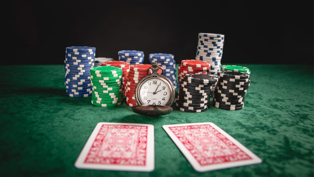 A stopwatch on a poker table with chips and two cards.