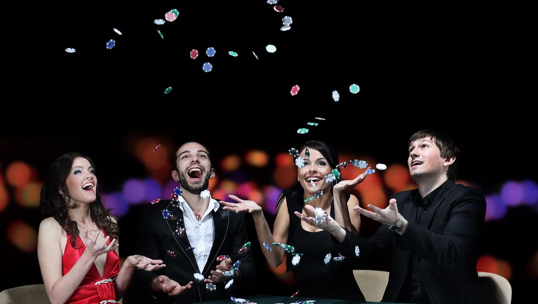 A group of young adults celebrates at the table by throwing poker chips in the air.