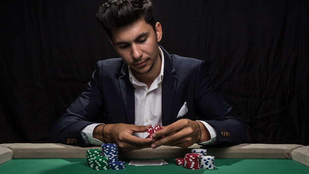 A serious-looking man in a suit sits at a poker table with chips in his hand.