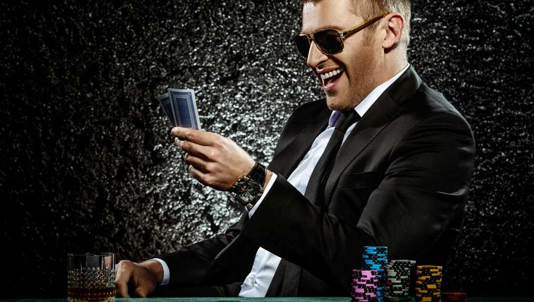 A poker player with a pile of casino chips at his elbow, smiles at his cards.