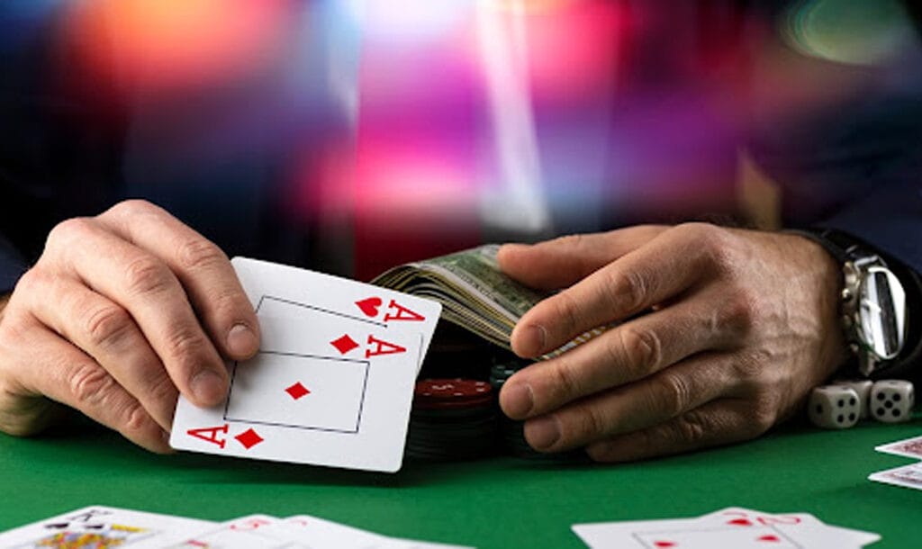 Poker player holding a pair of aces and money at a table with colorful lights in the background
