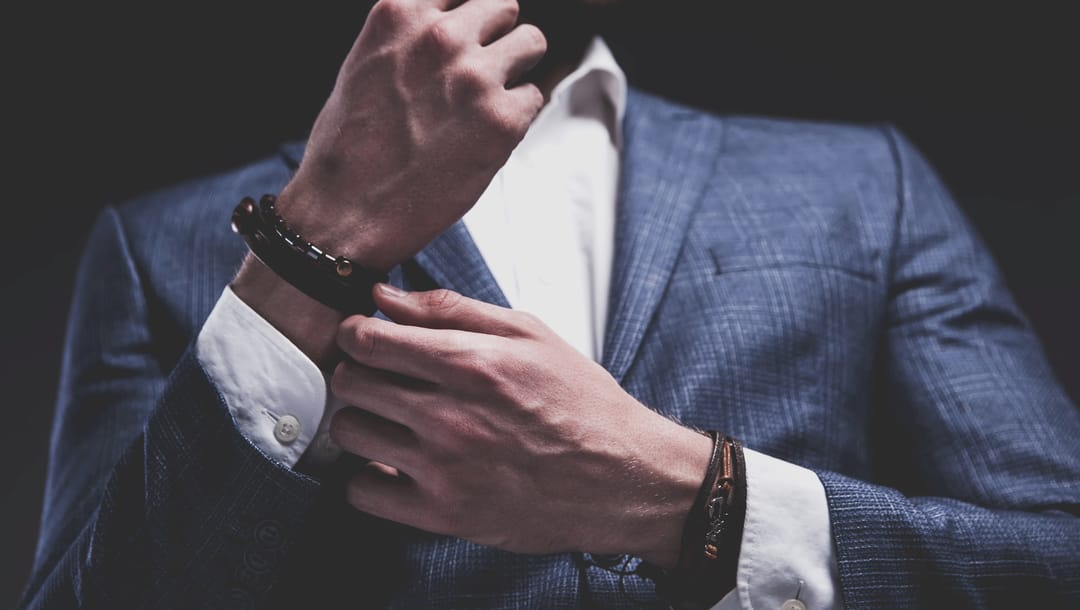 A man wearing a blue suit puts a bracelet on.