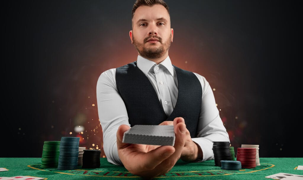 A male dealer presents a deck of cards at a poker table.