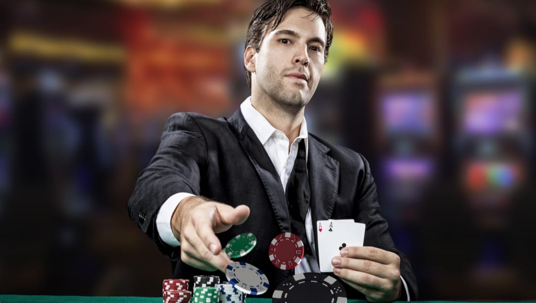 A poker player shows a pair of aces while tossing casino chips onto the table.