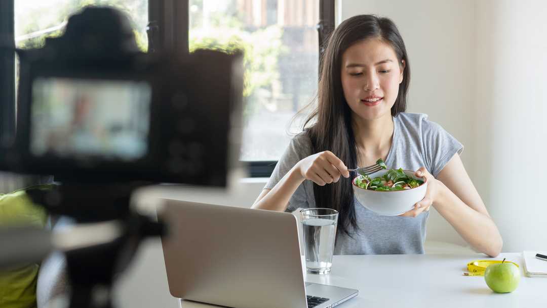A woman eats a healthy meal while sitting at a laptop.