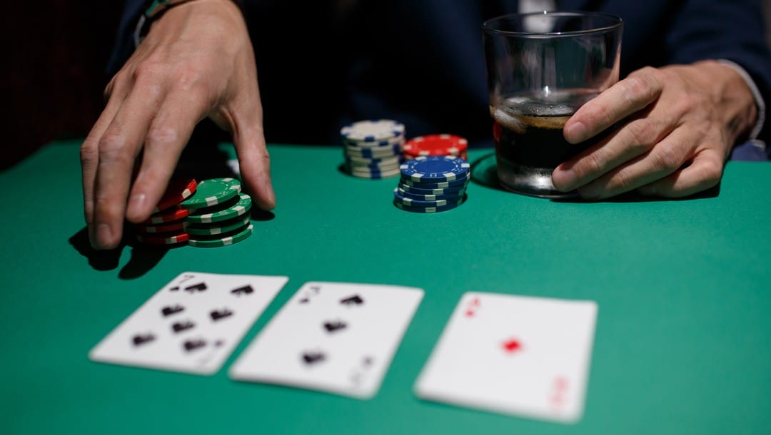 A poker player with a drink readies his wager.
