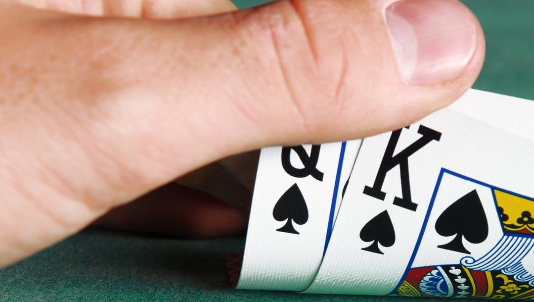 A poker player checks their hole cards. They see a king and a queen of spades.