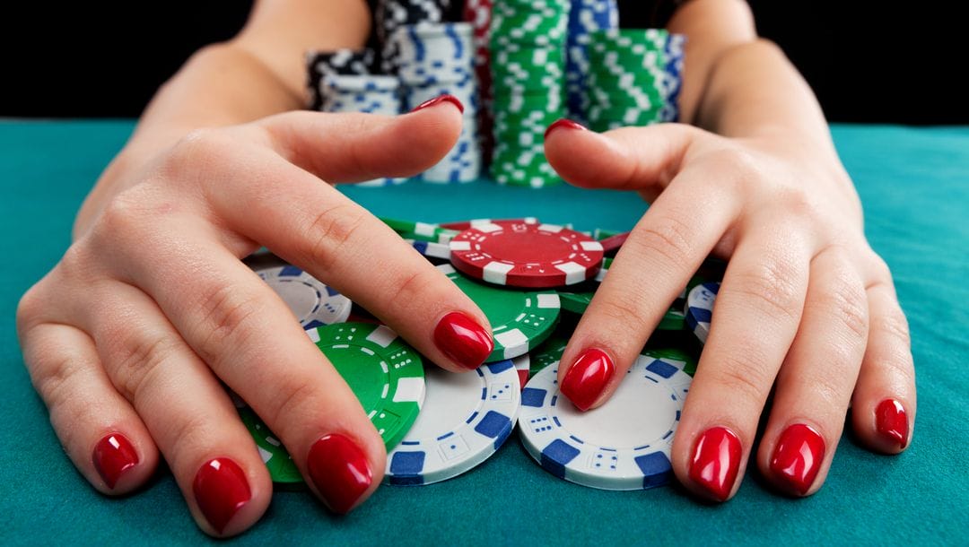 A woman pulls a poker pot towards her stacks of poker chips.