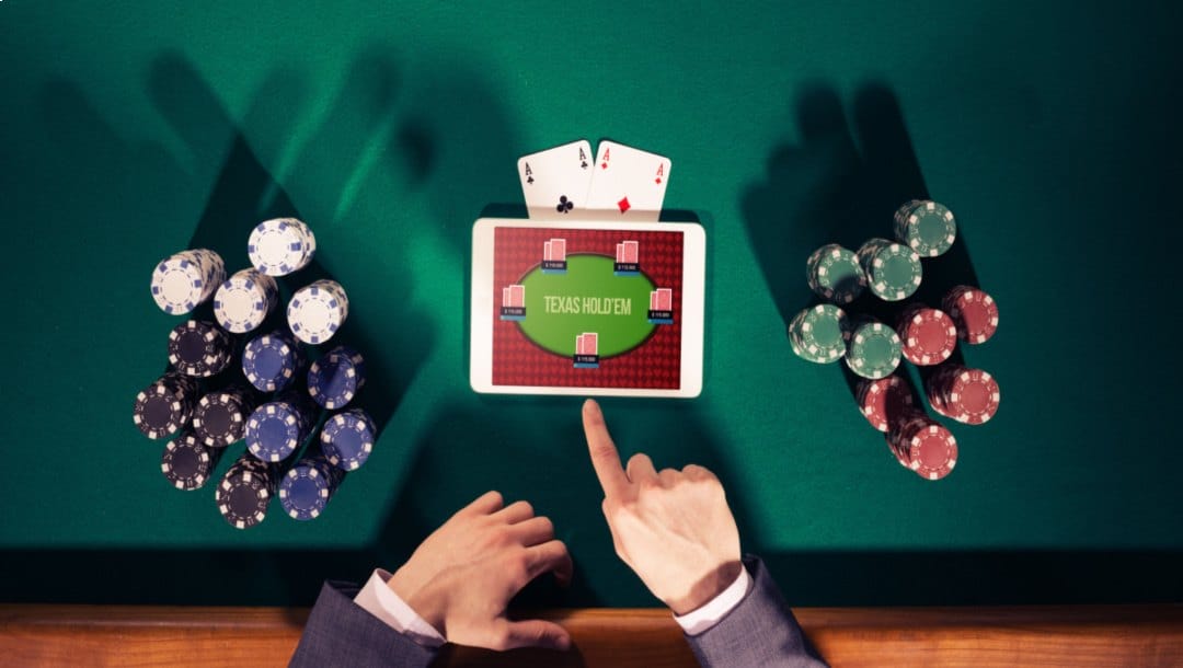 A poker player playing Texas Hold’em on a tablet with casino chips and playing cards.