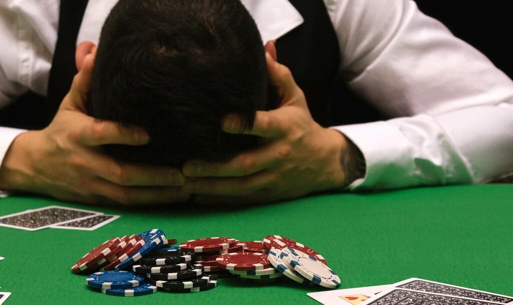 A poker player places his head in his hands on a poker table.