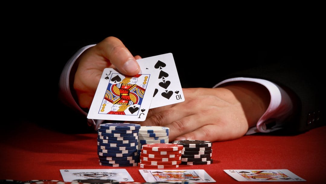 Poker player shows his cards over poker chips on a red felt table.