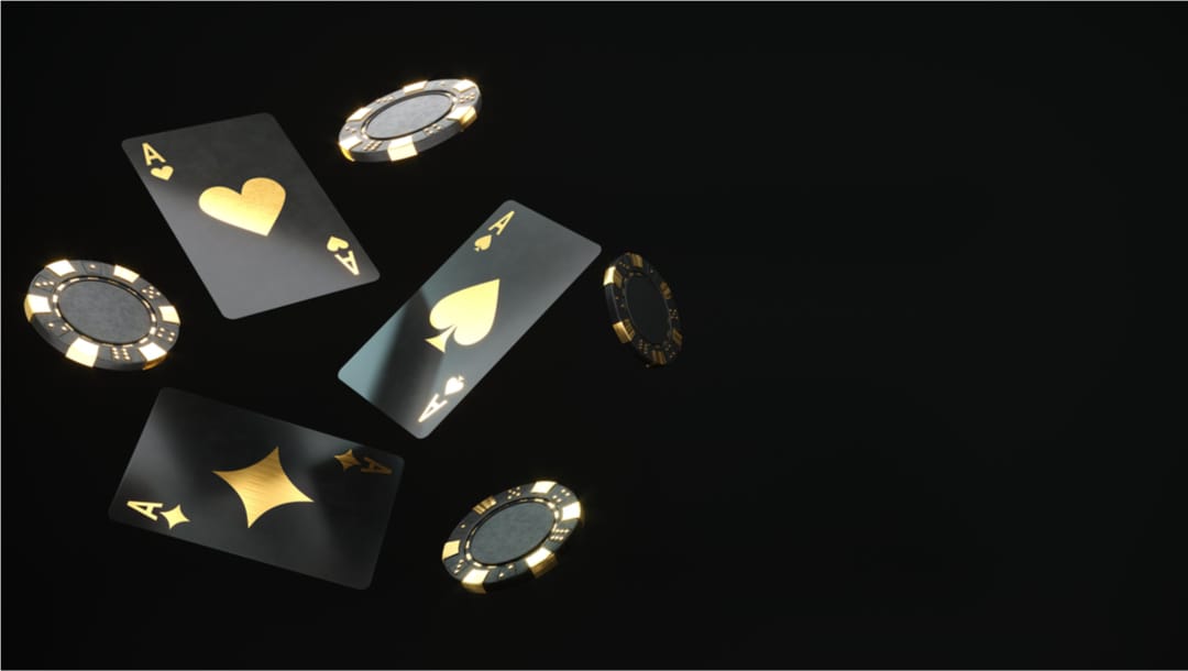 Black and gold playing cards and poker chips against black backdrop.