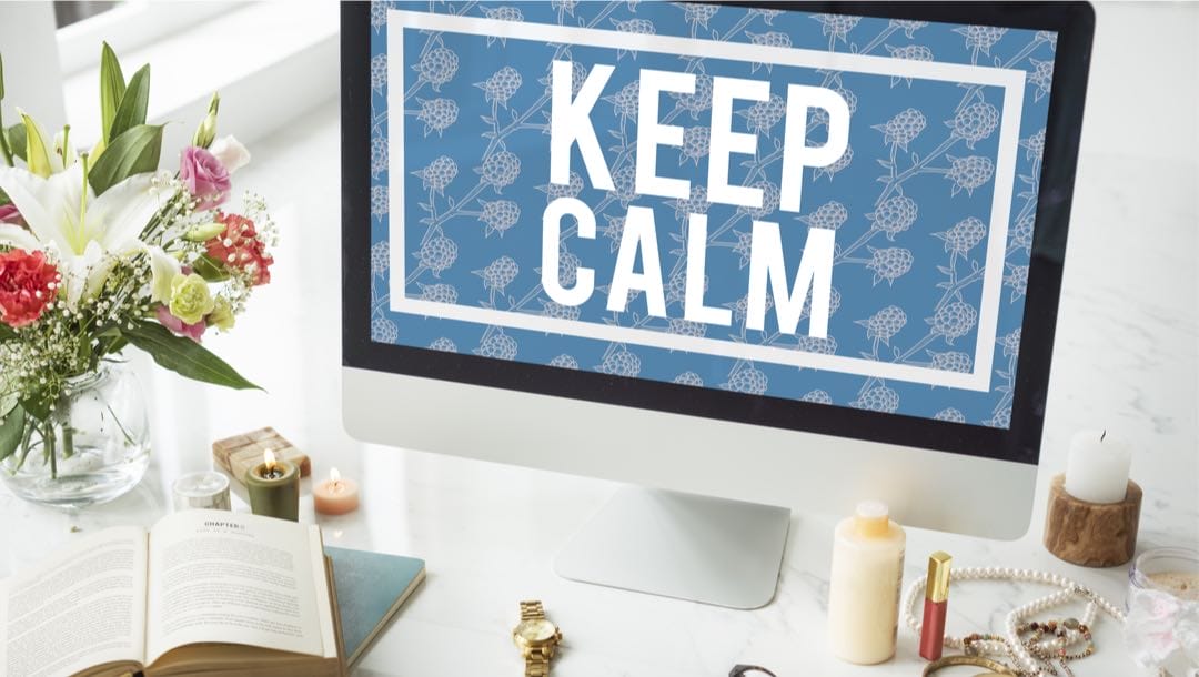 ‘Keep calm’ screensaver on a personal computer surrounded by candles, a book and flowers.