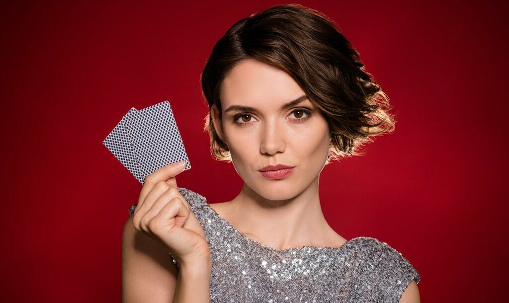 A woman wearing a sequin dress holding two playing cards against a red background.