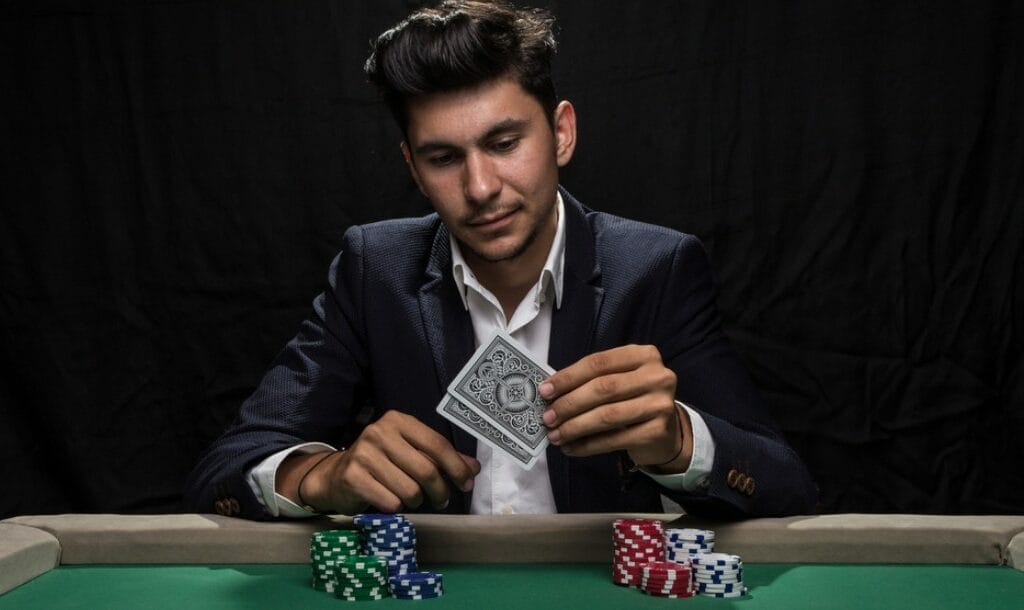 A poker player in a suit lifts his hole cards to check them.