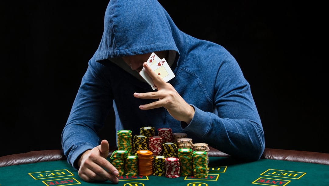 A poker player wearing a hoodie reveals his hole cards: a pocket pair of aces.