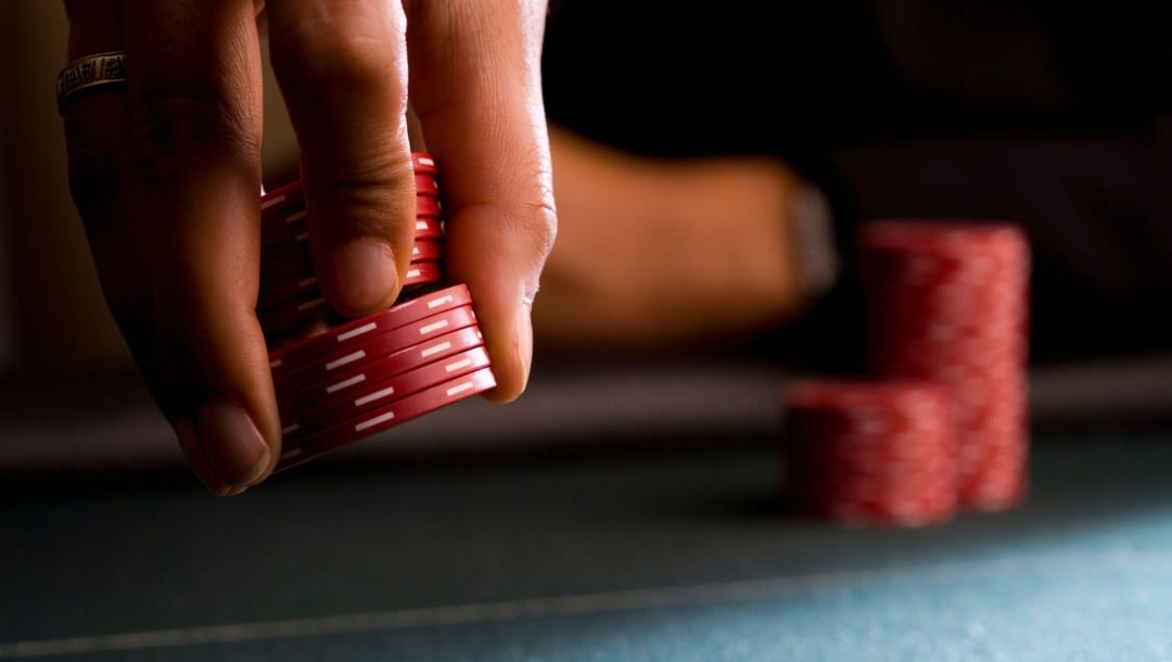 A woman holding red poker chips on a felt table.