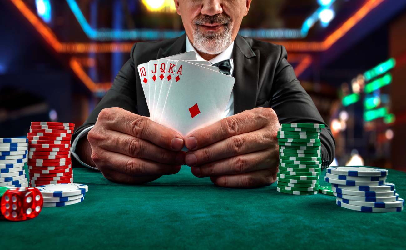 A poker player shows his poker hand on a green felt table with casino chips and dice.
