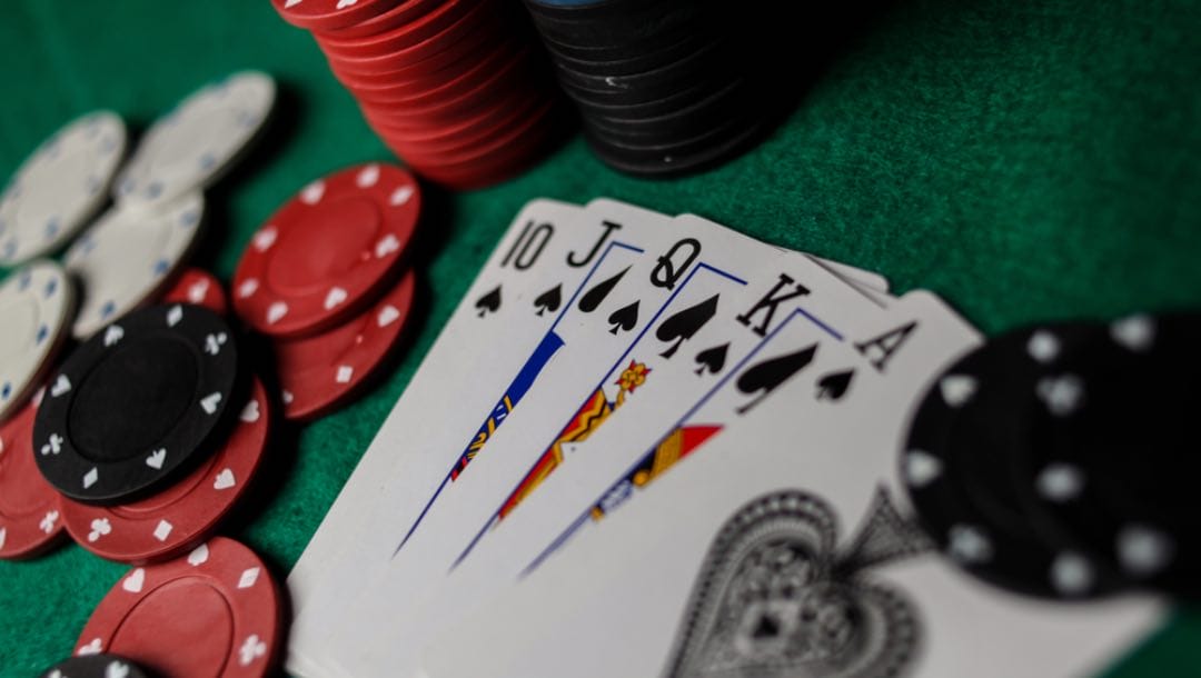 A royal flush of spades on a poker table next to some chips.