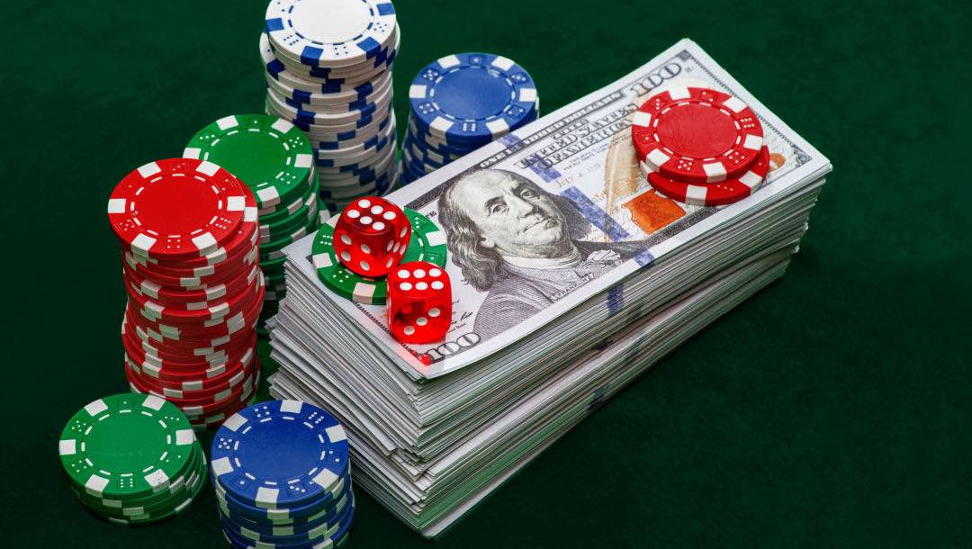 A tall stack of dollar bills surrounded by casino chips and dice.