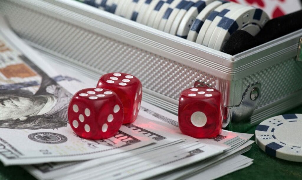 Dice, chips in a case and dollar bills on a green felt table.