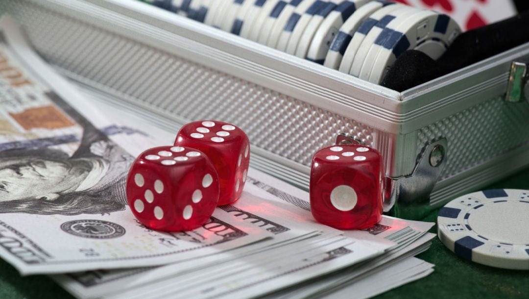Dice, chips in a case and dollar bills on a green felt table.