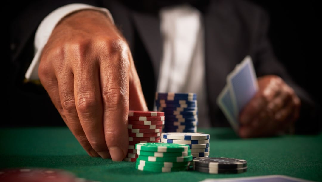 A man picks up a stack of chips on a green poker table.