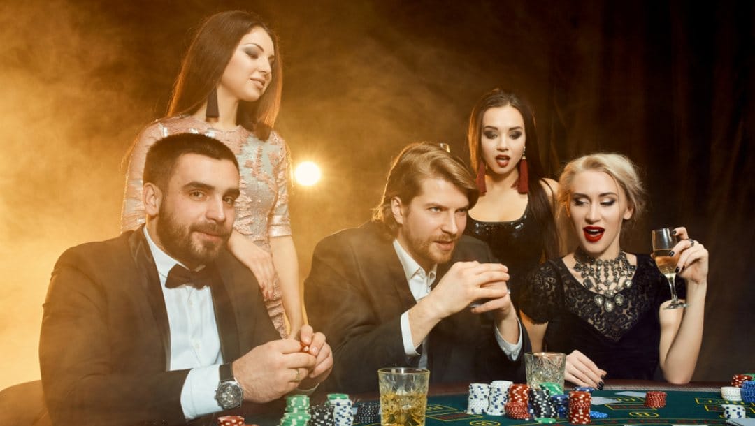 Three people take part in a game of poker with two women watching them play.