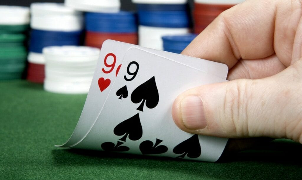 A poker player reveals their hole cards: a pair of nines.