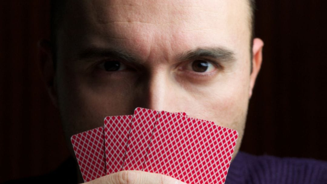 A poker player looks over the top of their hand of cards.
