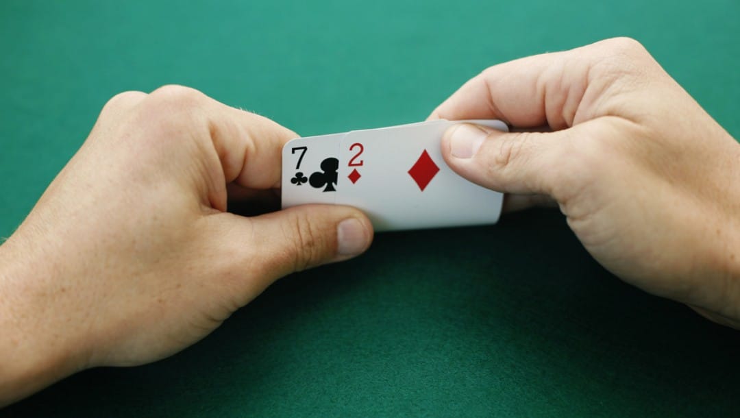 A poker player reveals their hole cards: an offsuit seven and a two.