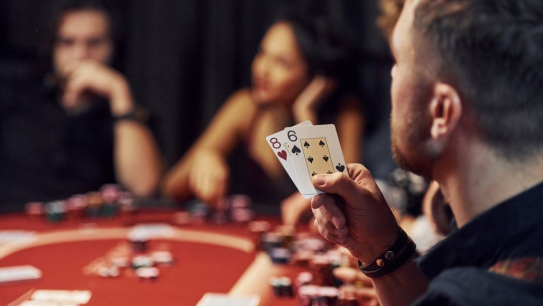 A man holds an 8 and 6 in his hand at the poker table.