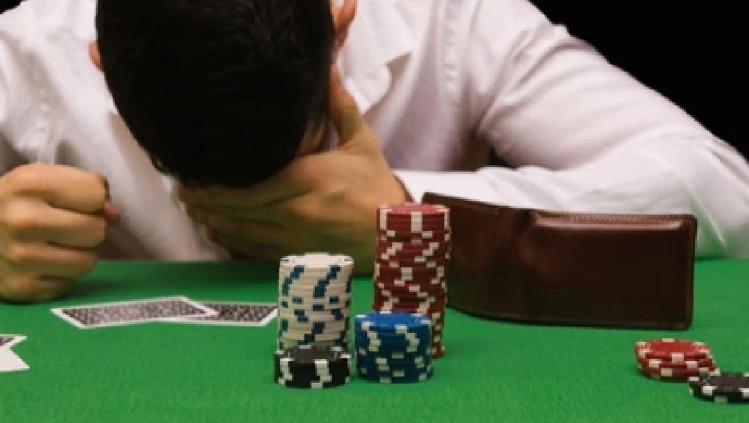 A man bowing his head in defeat at a poker table.