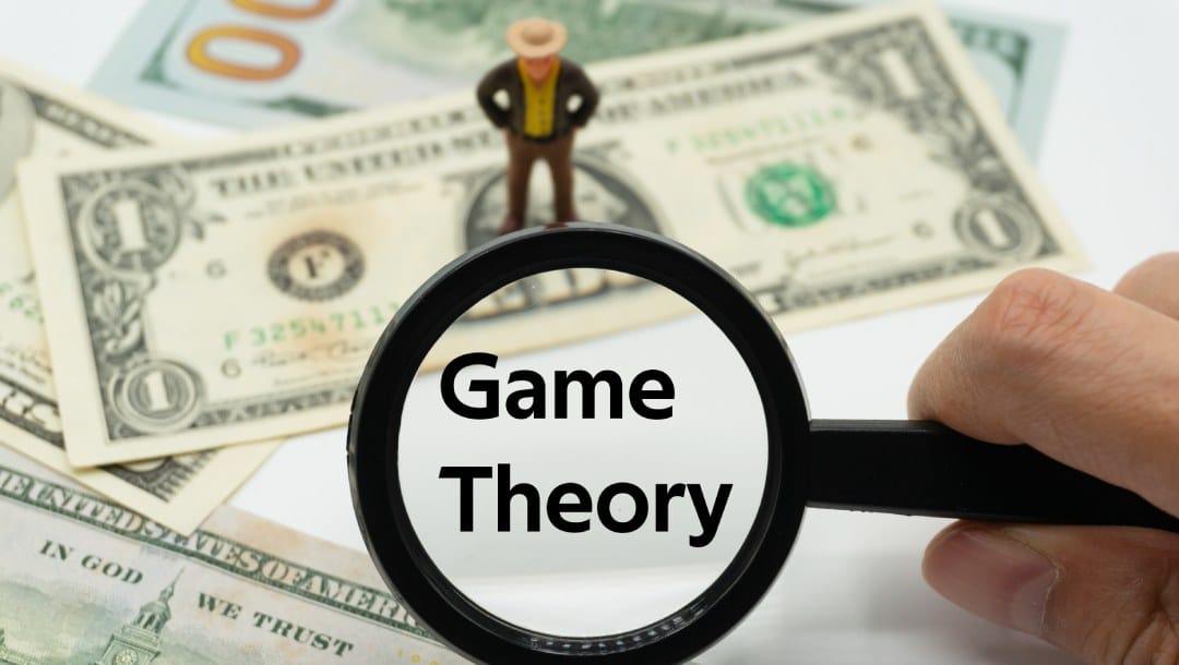 A magnifying glass enlarges the words “game theory” with banknotes in the background.