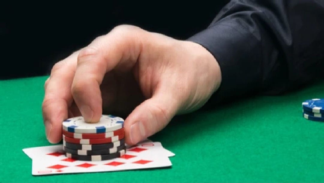 A man placing casino chips on a stack of cards.