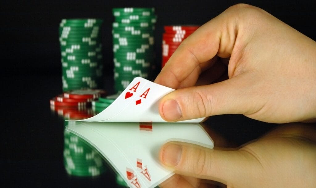 A hand revealing two ace poker cards in front of a stack of casino chips.